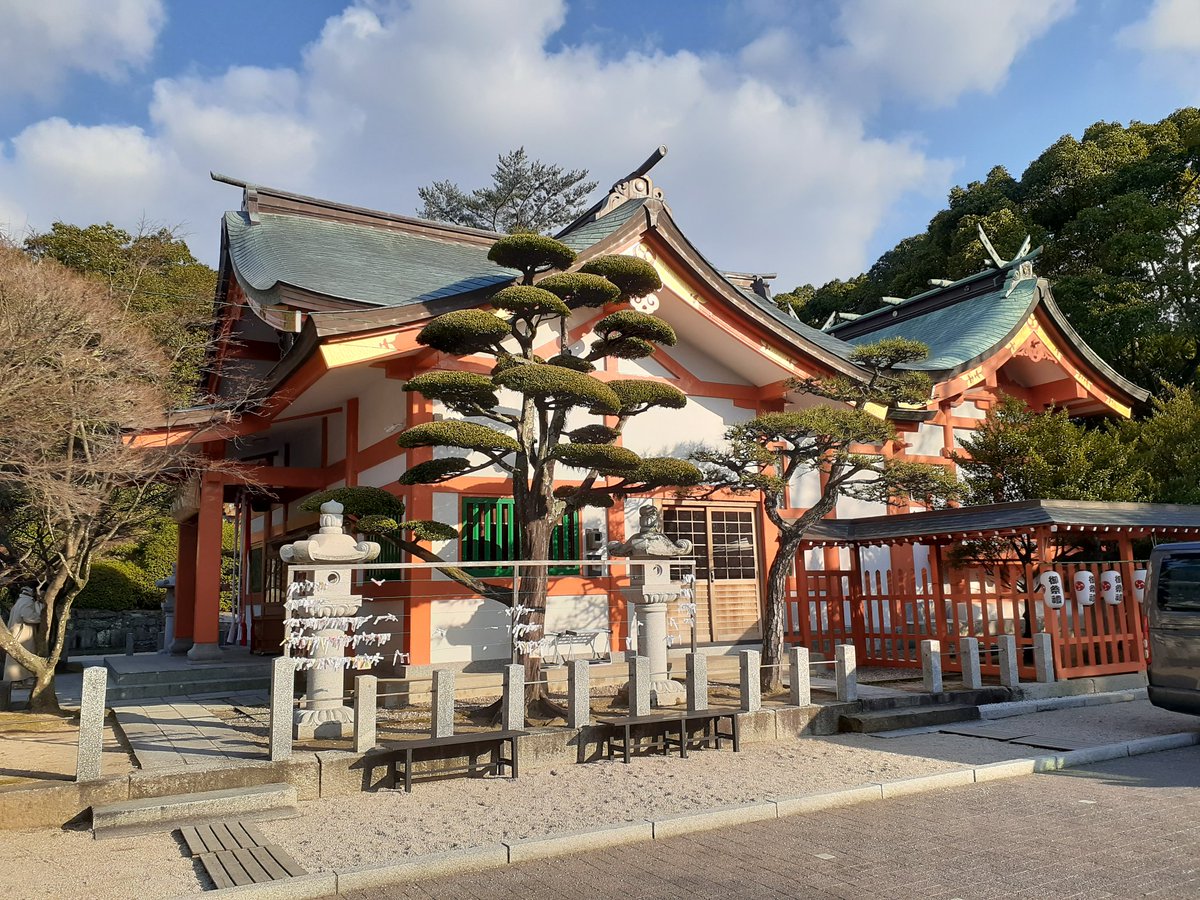 青空の下の、朱色の柱と緑の屋根の本殿