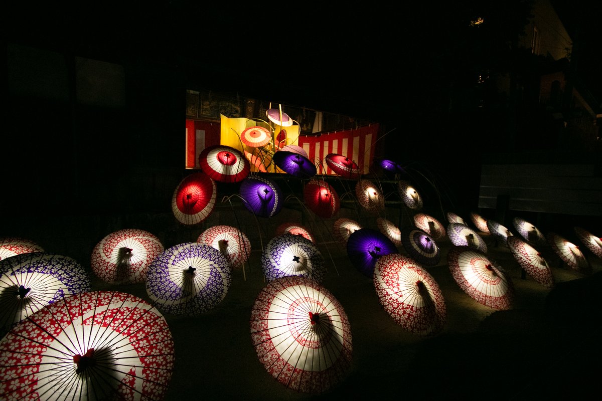 暗い境内に光る和傘が並び、奥に紅白の幕の舞台が見える